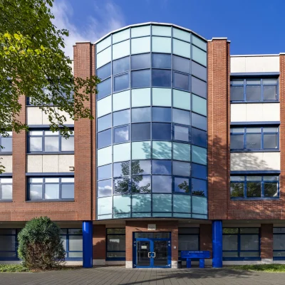 Zentrale Fassadenansicht eines Bürogebäudes an der Erkrather Straße in Düsseldorf mit verglastem Eingangsbereich, symmetrischer Architektur und blau akzentuierten Stützen.