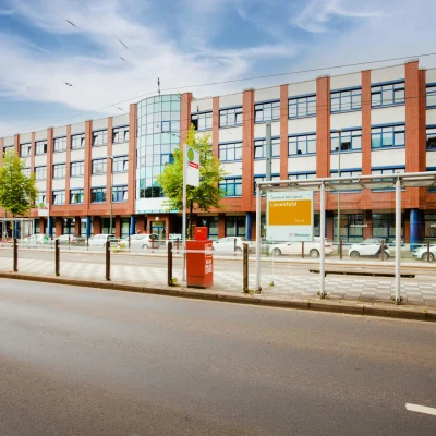 Straßenansicht eines Bürogebäudes an der Erkrather Straße in Düsseldorf mit Straßenbahnhaltestelle im Vordergrund, mehrgeschossiger Klinkerfassade und guter Anbindung an den öffentlichen Nahverkehr.