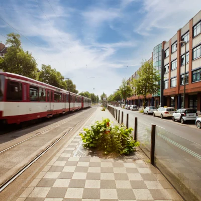 Blick entlang der Erkrather Straße in Düsseldorf mit Straßenbahngleisen, vorbeifahrender Bahn und angrenzendem Bürogebäude; urbane Lage mit direkter Verkehrsanbindung.