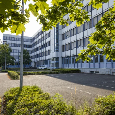 Blick auf das Büroensemble in der Konrad-Adenauer-Straße in Köln mit angrenzenden Stellplätzen, klar strukturierter Fassade und begrüntem Umfeld.