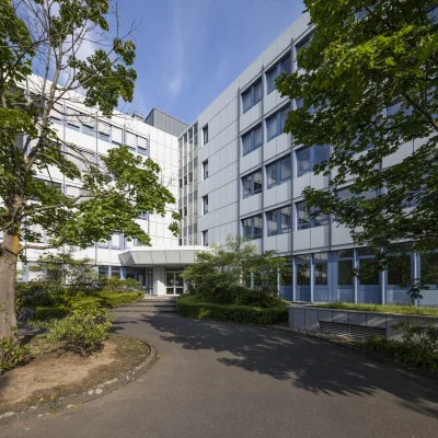 Außenansicht eines Bürogebäudes in der Konrad-Adenauer-Straße in Köln mit begrüntem Innenhof, modernen Fassadenelementen und zentralem Eingangsbereich.