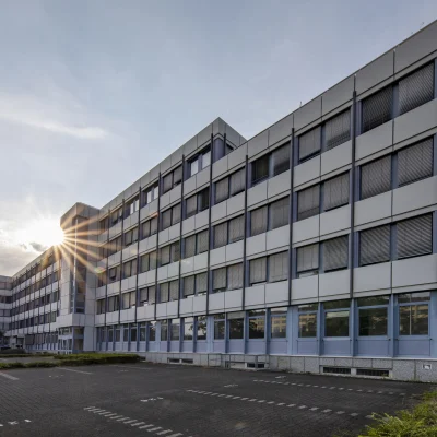 Außenansicht eines Bürogebäudes in der Konrad-Adenauer-Straße in Köln bei tiefem Sonnenstand mit Lichtreflexionen auf der Fassade und ruhigem Außenbereich.
