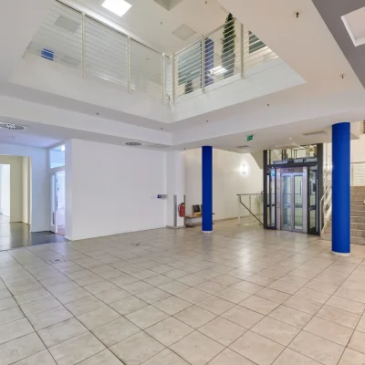 Großzügiges Foyer eines Bürogebäudes in der Marburger Straße in Berlin mit Aufzug, Treppenanlage, blauen Stützen und gefliestem Boden.