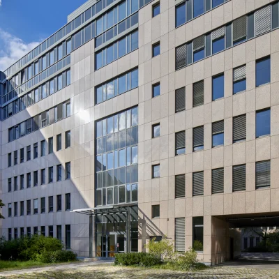 Außenansicht eines modernen Bürogebäudes in der Soorstraße in Berlin mit heller Natursteinfassade, großen Fensterflächen und verglastem Haupteingang, umgeben von begrünten Außenbereichen.