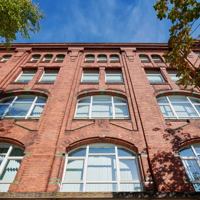 Detailansicht der historischen Backsteinfassade der Erlenhöfe Berlin mit großen Rundbogenfenstern, dekorativen Zierelementen und klassischer Industriearchitektur unter blauem Himmel.