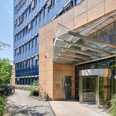 Überdachter Eingangsbereich des Bürogebäudes Kaiserin-Augusta-Allee 104–106 mit Glasvordach und gepflegter Außenanlage.