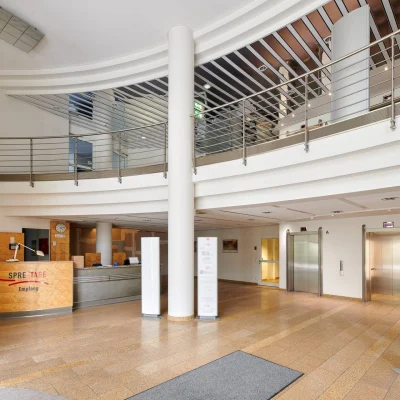 Helle und repräsentative Empfangshalle des Bürogebäudes Kaiserin-Augusta-Allee 104–106 mit Galerie, Aufzügen und zentralem Empfangsbereich.