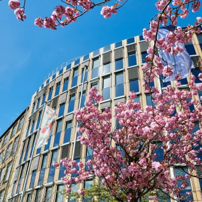 Außenansicht des Bürogebäudes Kaiserin-Augusta-Allee 104–106 in Berlin mit moderner Fassadengestaltung und blühenden Bäumen im Vordergrund.