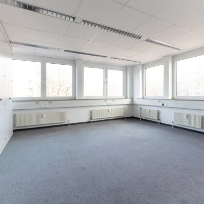 Heller Büroraum mit großzügigen Fensterfronten, neutralem Bodenbelag und angenehmer Arbeitsatmosphäre.