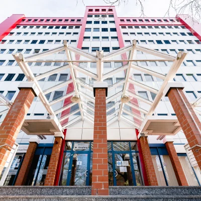Repräsentativer Eingangsbereich eines Bürogebäudes in Hannover mit markanter Glasüberdachung, Backsteinpfeilern und moderner Fassadengestaltung vor einem mehrgeschossigen Gebäude.