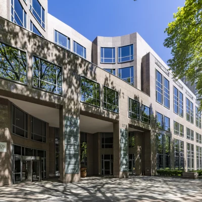 Großzügige Gesamtansicht eines Büroensembles mit Natursteinfassade, Glasflächen und altem Baumbestand an der Kaiserswerther Straße in Düsseldorf.