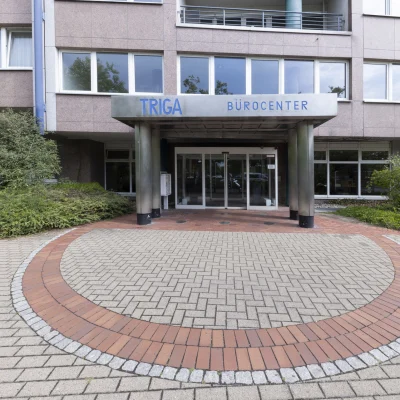 Haupteingang des TRIGA Bürocenters mit überdachtem Portal, automatischen Glastüren und klarer Adresswirkung.