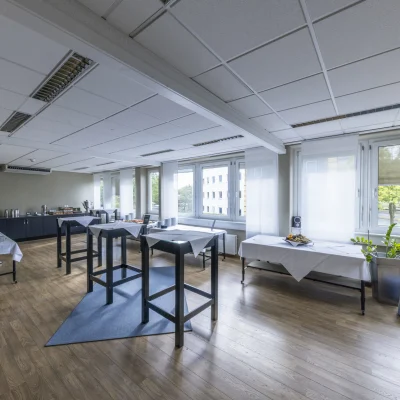 Heller Innenbereich mit Stehtischen, Cateringzone und großen Fensterflächen, geeignet für Meetings, Events oder Pausenformate.