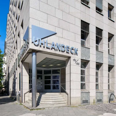 Repräsentativer Haupteingang des Bürogebäudes Uhlandeck in Berlin mit markantem Gebäudeschriftzug und großzügigem Vorplatz.