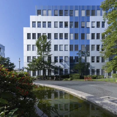 Bürogebäude mit Wasserfläche und Gehweg in grüner Umgebung