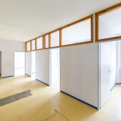 Flurbereich einer leerstehenden Bürofläche mit Glaswänden, Holzoptik-Boden und moderner Deckenbeleuchtung in der Antoniterstraße 33 in Frankfurt.