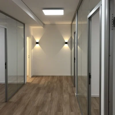 Flurbereich einer leerstehenden Bürofläche mit Glaswänden, Holzoptik-Boden und moderner Deckenbeleuchtung in der Antoniterstraße 33 in Frankfurt.