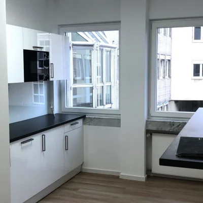 Helle Teeküche innerhalb einer Bürofläche mit weißen Einbauten, dunkler Arbeitsplatte und Fenster in der Antoniterstraße 33 in Frankfurt.