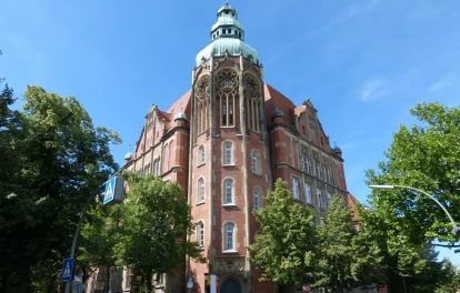 Seitliche Außenansicht der historischen Gewerbeimmobilie in der Bergstraße 1 in Berlin mit roter Backsteinfassade und umgebendem Baumbestand.