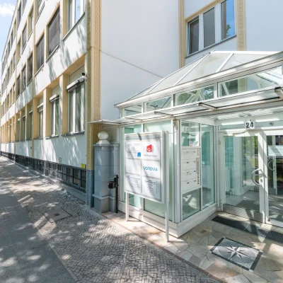 Verglaster Eingangsbereich der Büroimmobilie Heerstraße 24 in Berlin mit Glasüberdachung an einer begrünten Straße.