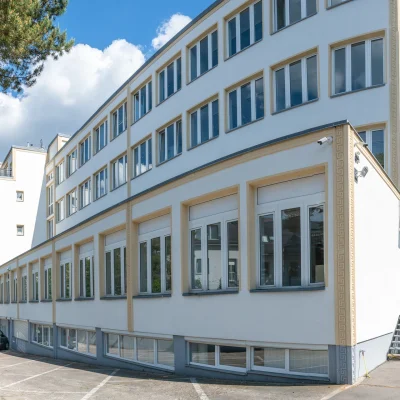 Außenansicht der Büroimmobilie Heerstraße 24 in Berlin mit heller Fassade, Fensterfronten und angrenzenden Parkplätzen.