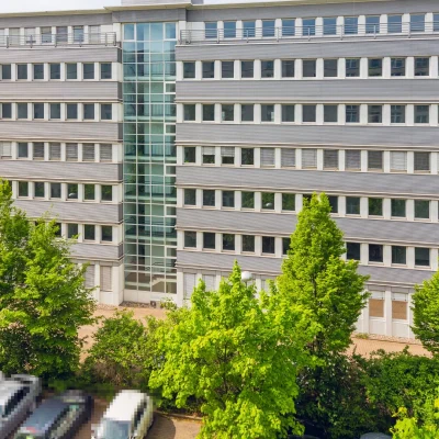 Fassadenansicht des Bürocenter Weidetor mit Glasaufzugsturm und Grünflächen