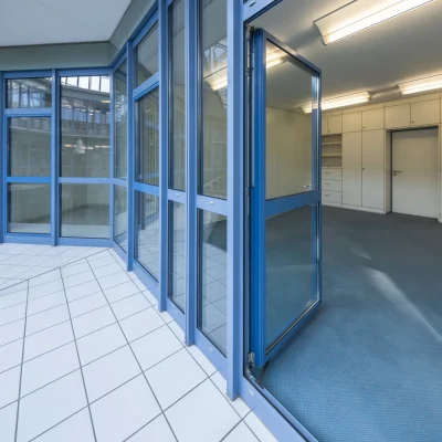 Verglaster Flur mit blauen Rahmen und Blick in ein Büro mit Einbauschränken und Empfangstheke