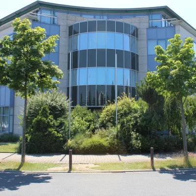 Bürogebäude mit markanter Rundglasfassade, umgeben von Bäumen an einem Sommertag