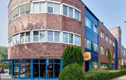 Backsteingebäude mit runder Ecke, Glasvordach und blauer Fassadenverglasung