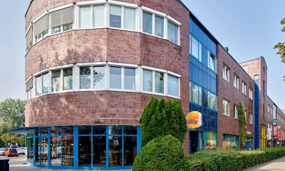 Backsteingebäude mit runder Ecke, Glasvordach und blauer Fassadenverglasung