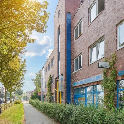 Backsteingebäude mit blauen Fensterrahmen entlang einer baumgesäumten Straße
