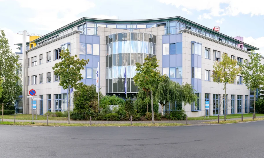 Bürogebäude mit runder Glasfront, Natursteinfassade und Grünanlage bei bewölktem Himmel