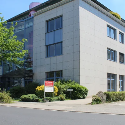 Eckansicht des Bürogebäudes mit Glaseingang, Vordach und gepflegter Grünbepflanzung