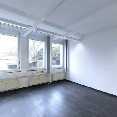Leerer Büroraum mit Blick ins Grüne und umlaufender Deckenbeleuchtung