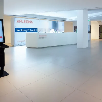 Weitläufige Empfangshalle mit langem Tresen, Check-in-Terminal und heller Bodenfliesen