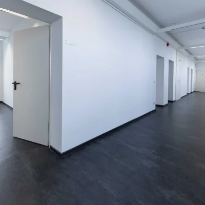 Heller Flur mit dunklem Bodenbelag, offener Bürotür und Fensterband