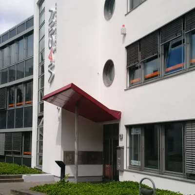 Gebäudeeingang mit rotem Vordach und markanten Rundfenstern an der Fassade