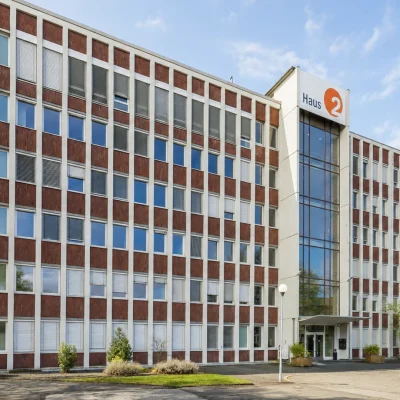 Bürogebäude Haus 2 mit Klinkerfassade, Glaseingang und Bäumen im Frühling