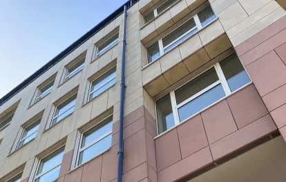 Fassadendetail mit beige-rosa Fliesen und Fensterreihen von unten fotografiert