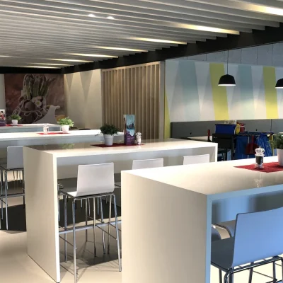 Kantine mit weißen Stehtischen, Barhockern und farbig gestalteter Wand