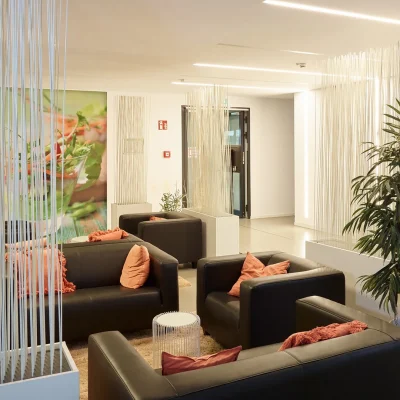 Lounge mit schwarzen Ledersofas, Raumteilern und Grünpflanze neben der Kantine