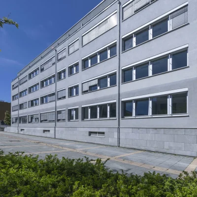 Graue Bürogebäudefassade mit Fensterreihen und Sonnenschutzlamellen bei blauem Himmel