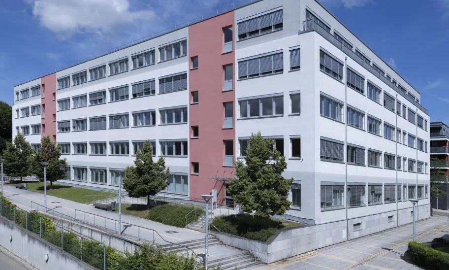 Weitwinkelansicht des Bürogebäudes mit rotem Fassadenakzent und Vorplatz