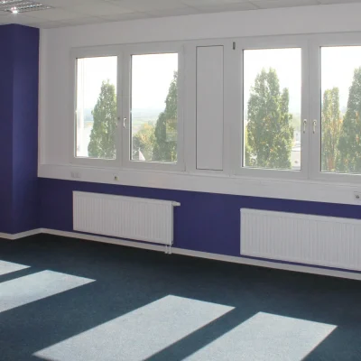 Leeres Büro mit violetter Wandgestaltung, Schreibtisch und Fensterfront