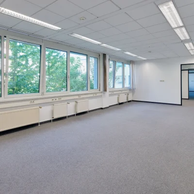 Leeres Großraumbüro mit Fensterfront, Teppichboden und Tür zum Flur