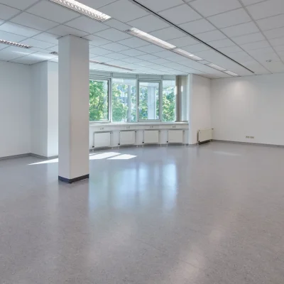 Leerer Büroraum mit Säule, Fensterfront und Vorhängen bei Tageslicht