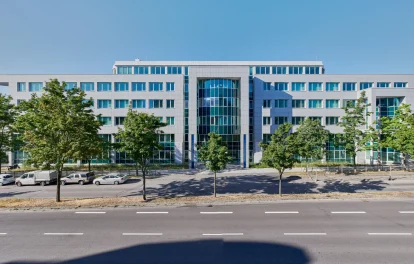 Bürogebäude mit Steinfassade, Bäumen und Parkplätzen an der Straße
