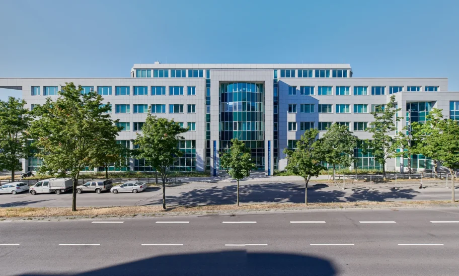Bürogebäude mit Steinfassade, Bäumen und Parkplätzen an der Straße