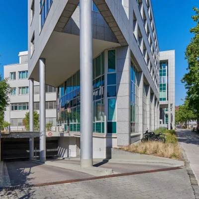 Moderne Gebäudeecke mit Stützpfeilern und Glasfassade an der Tiefgarageneinfahrt