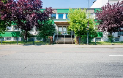 Bürogebäude mit grüner Fassade hinter blühenden Bäumen an der Straße